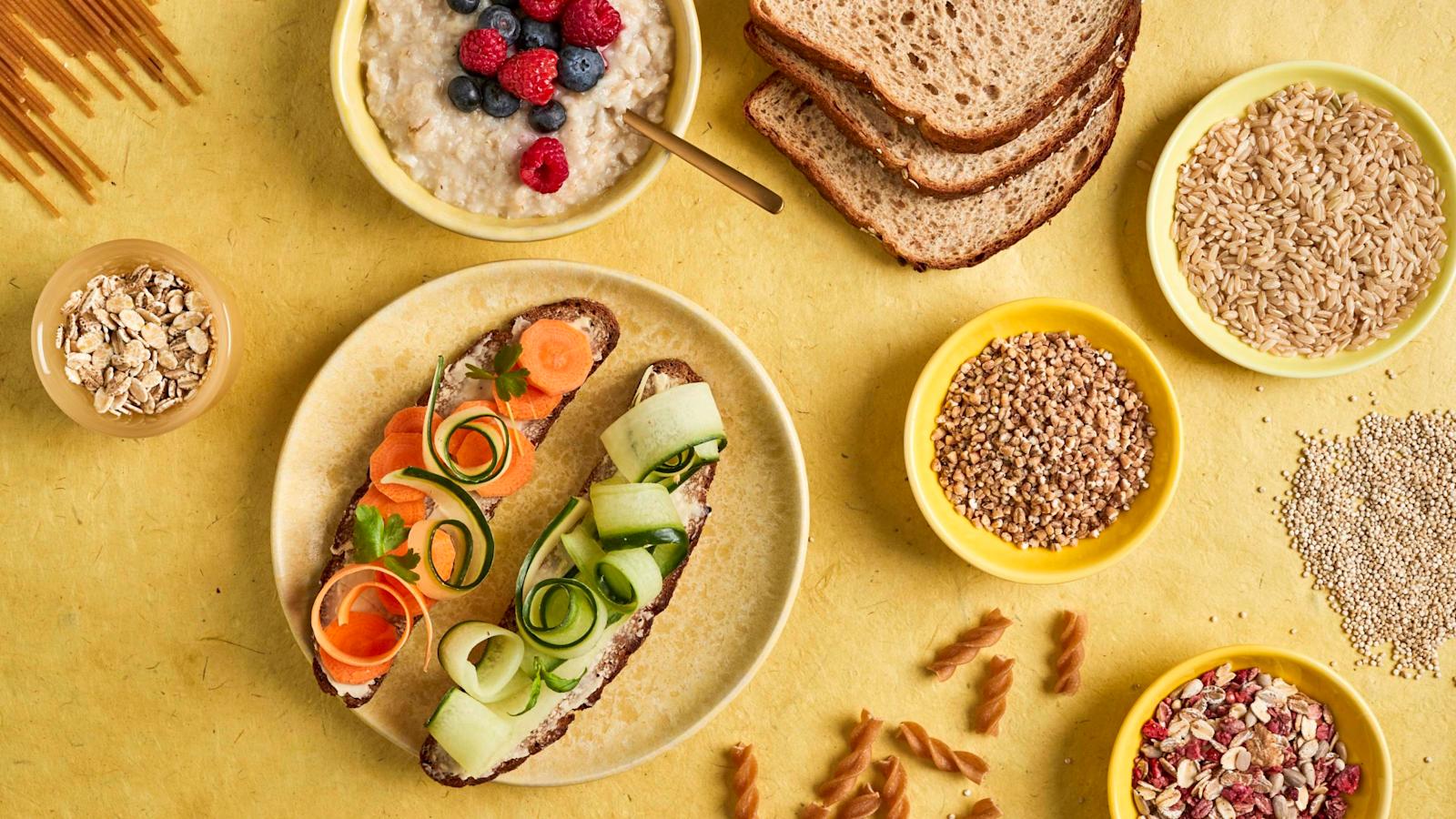 Keltaisella taustalla keltaisia lautasia, joilla leipiä, puuroa ja muita täysjyvätuotteita.