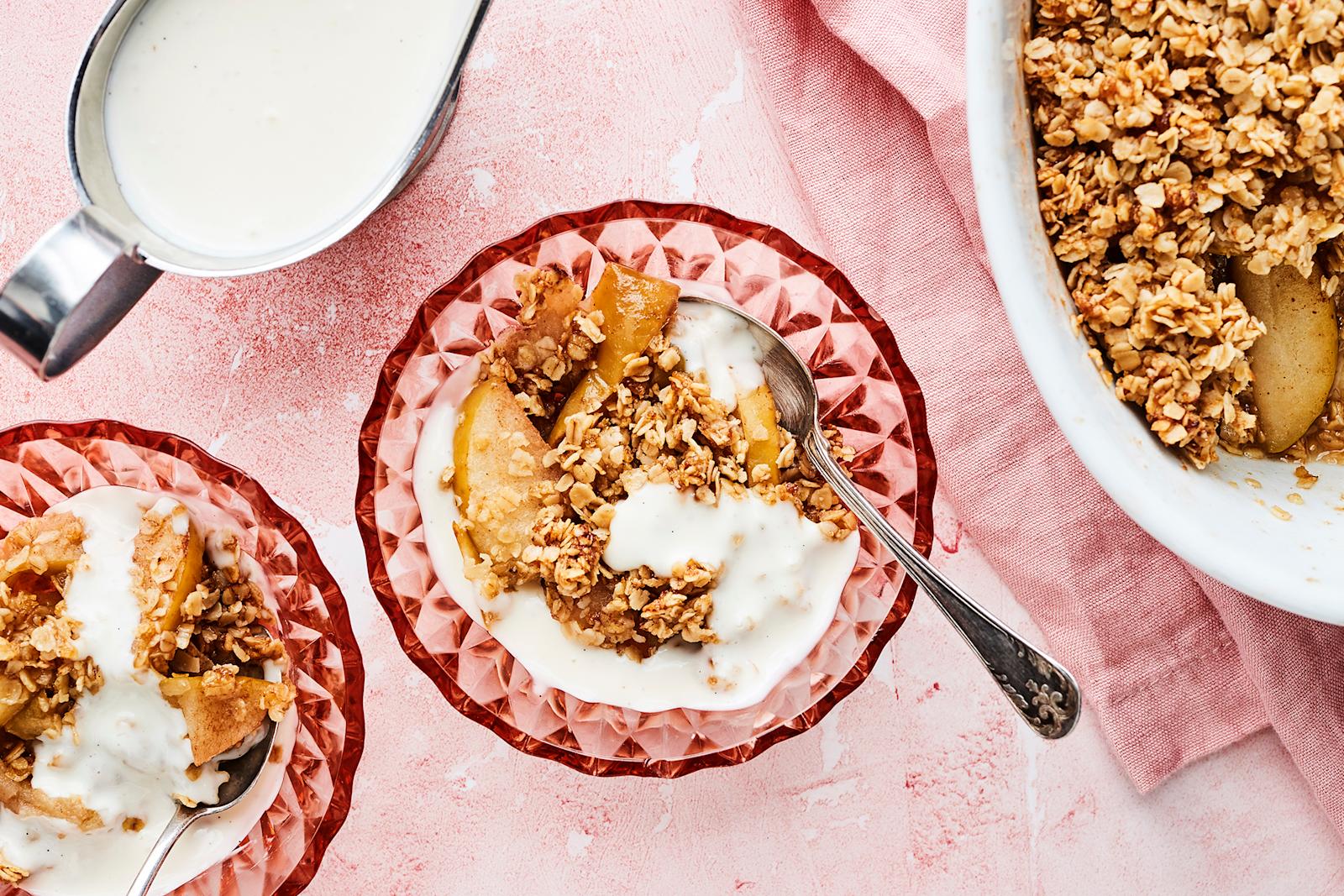 Kaura-omenapaistosta kahdessa lasikulhossa ja uunivuoassa. Uunivuoan alla vaaleanpunainen liina. Vanijakastiketta kastikekannussa.