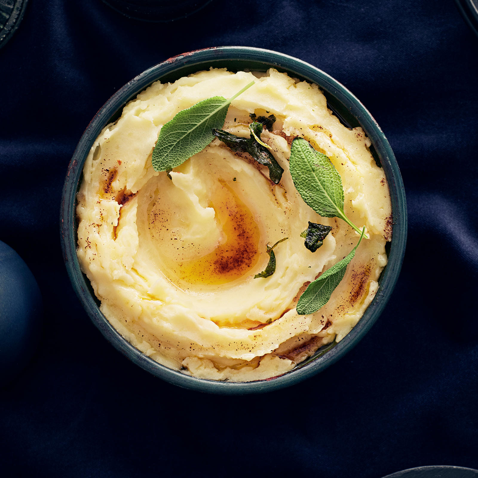 Kulhossa perunamuusia, jonka päällä salviavoita ja salvianlehtiä. Vieressä kastikekannu, jossa salviavoita.