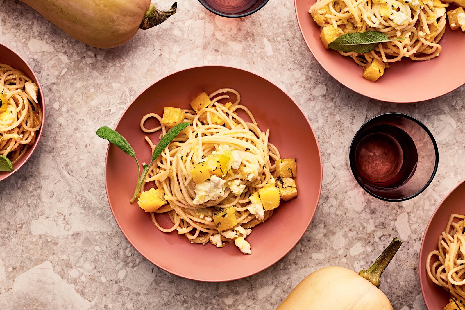 Kurpitsa-uunifetapastaa neljällä lautasella. Kaksi myskikurpitsaa ja vesilasia.