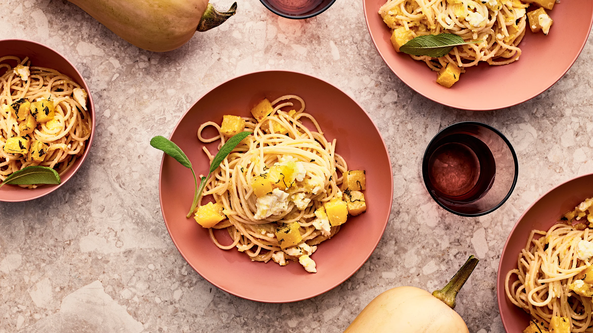 Kurpitsa-uunifetapastaa neljällä lautasella. Kaksi myskikurpitsaa ja vesilasia.