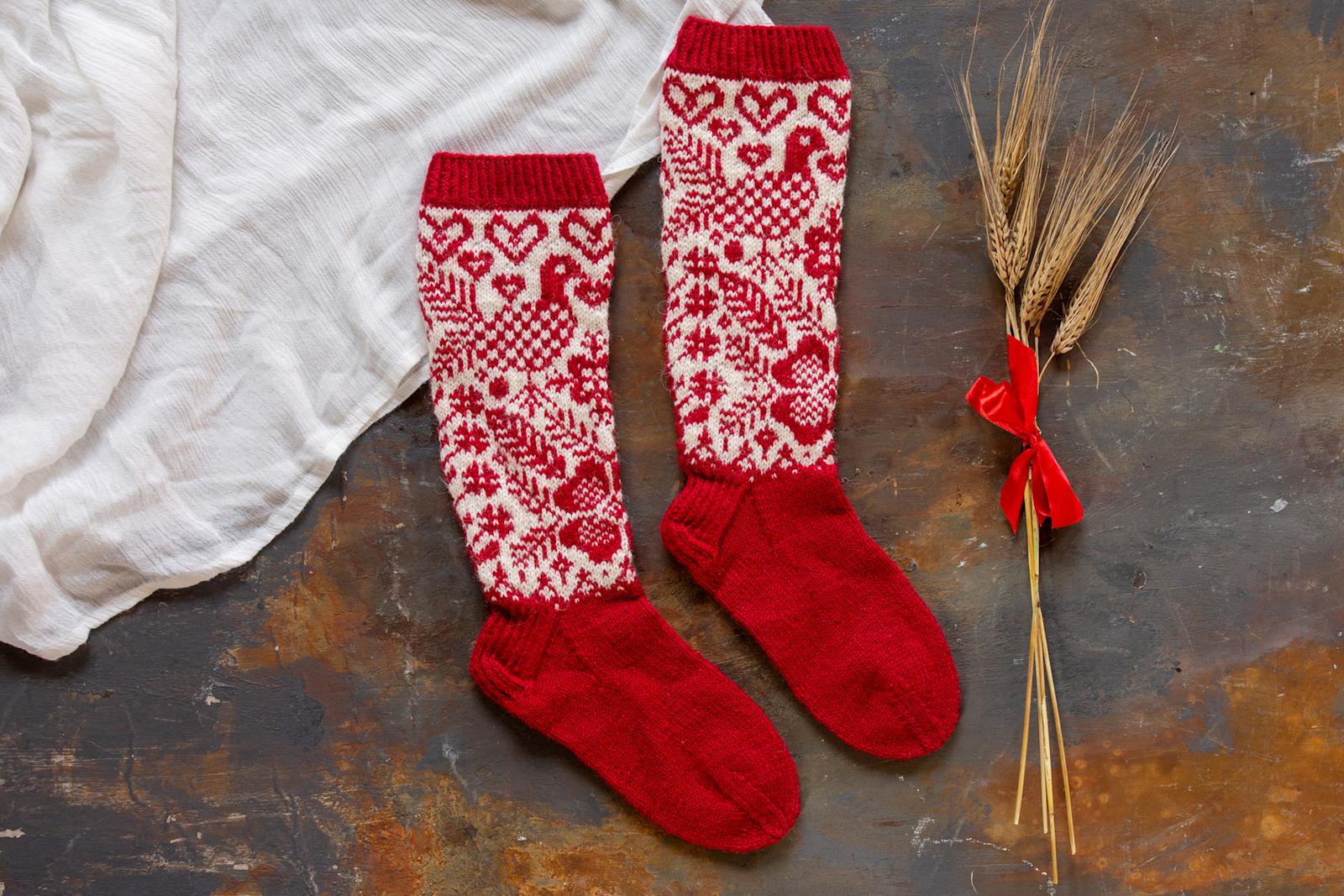 Kuvassa punavalkoiset pitkävartiset villasukat, joita koristavat käki ja karjalanruusu.
