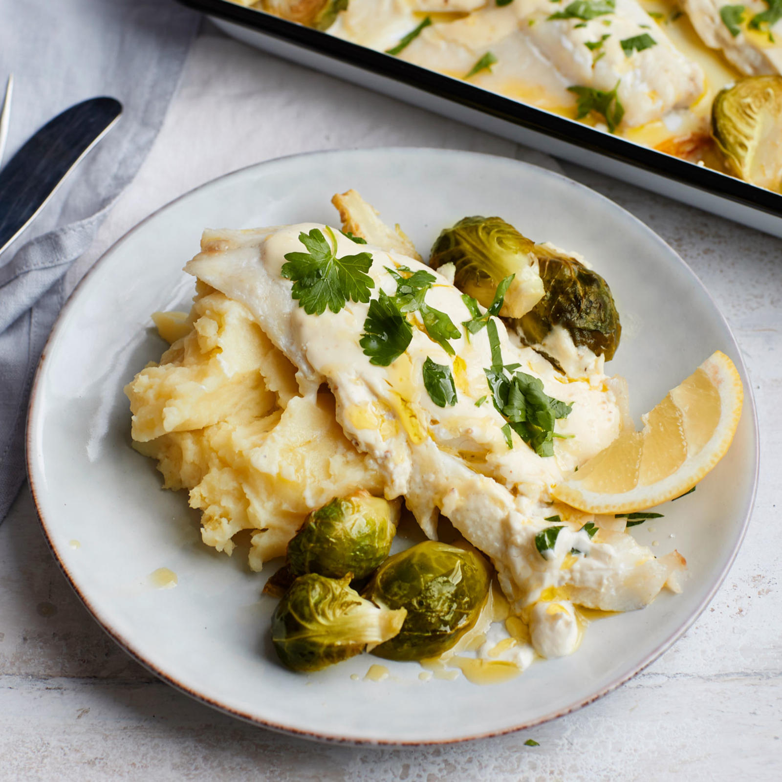 Smetanakuorrutteinen kuhafilee lautasella perunamuusin, ruusukaalien ja sitruunan kera