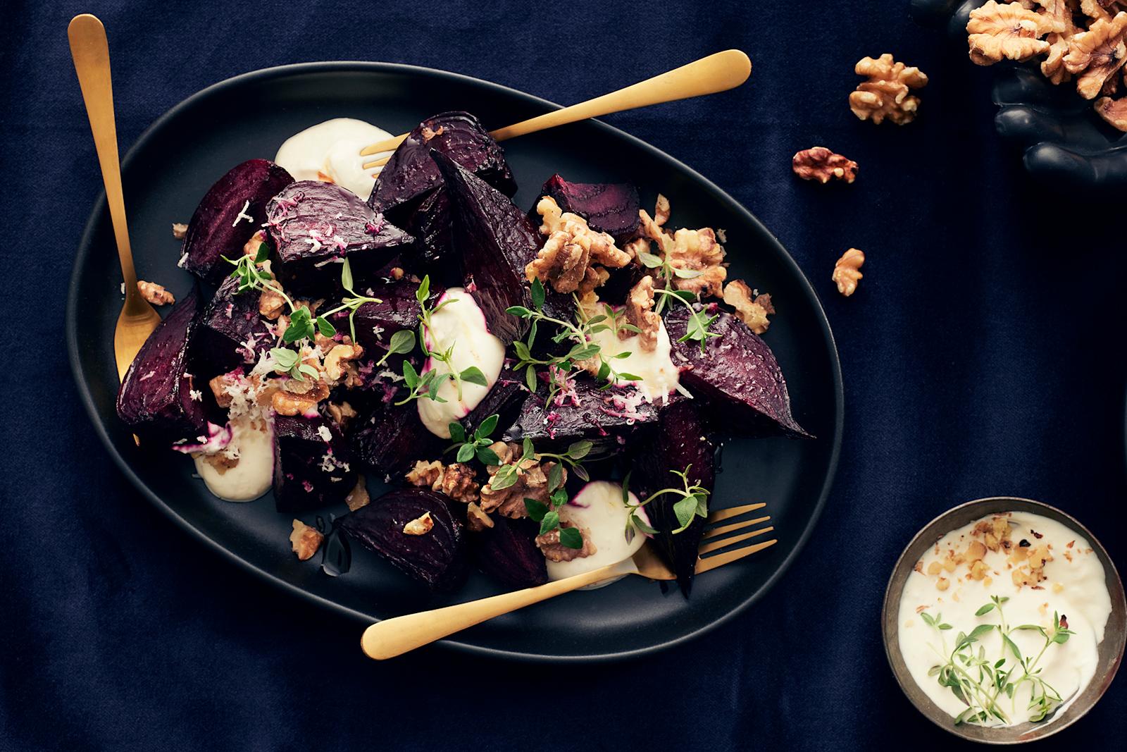 Paahdettuja punajuuria tummalla tarjoiluastialla piparjuurikastikkeella, saksanpähkinöillä ja timjamilla koristeltuna. Lautasella kolme haarukkaa. Lautasen vieressä saksanpähkinöitä ja piparjuurikastiketta kulhossa.