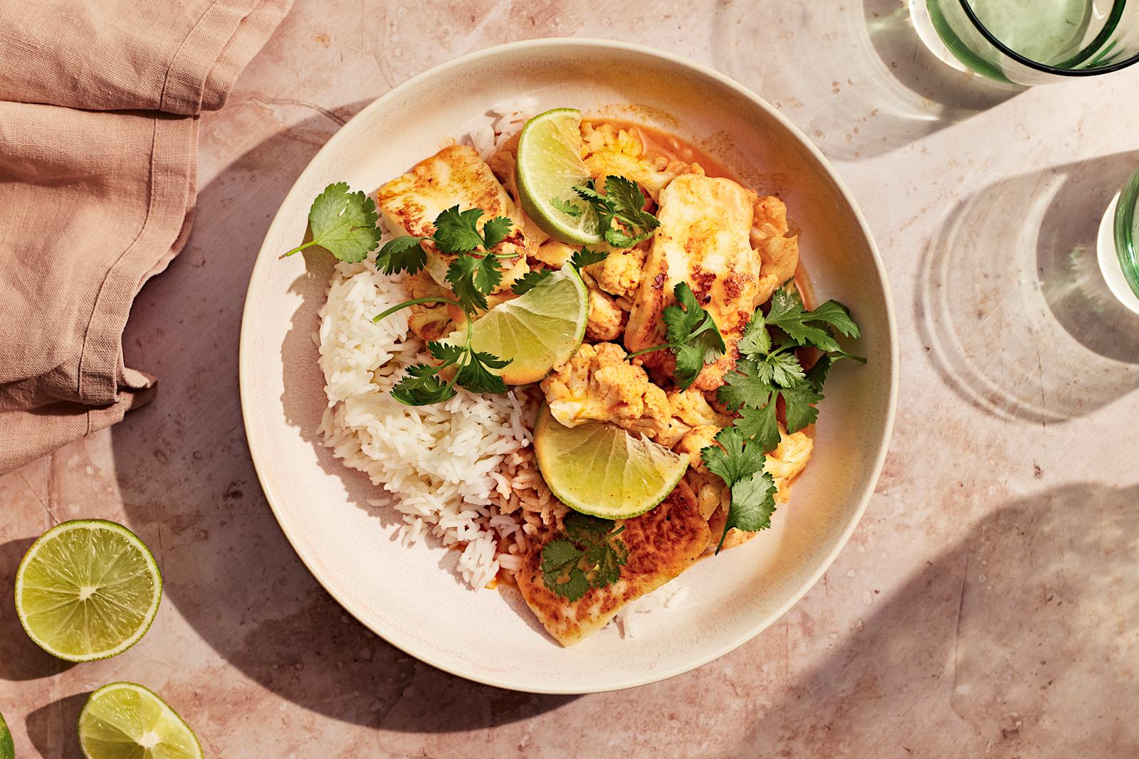 Halloumicurry ja riisiä limellä ja korianterilla koristeltuna. Annoksen vieressä vesilaseja, limejä ja beige liina.