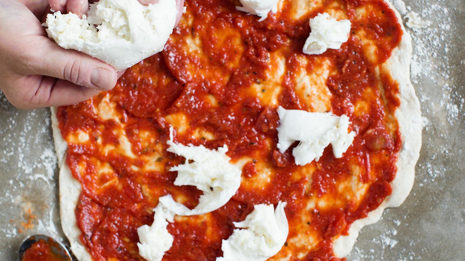 4\. Levitä tomaattikastike pohjalle. Revi peh-meää mozzarellaa sinne tänne tomaattikastikkeen päälle. Älä peitä koko pizzaa juustolla! Lisää muutama kirsikkatomaatti. Pakasta ylijäänyt kastike seuraavaa kertaa varten.