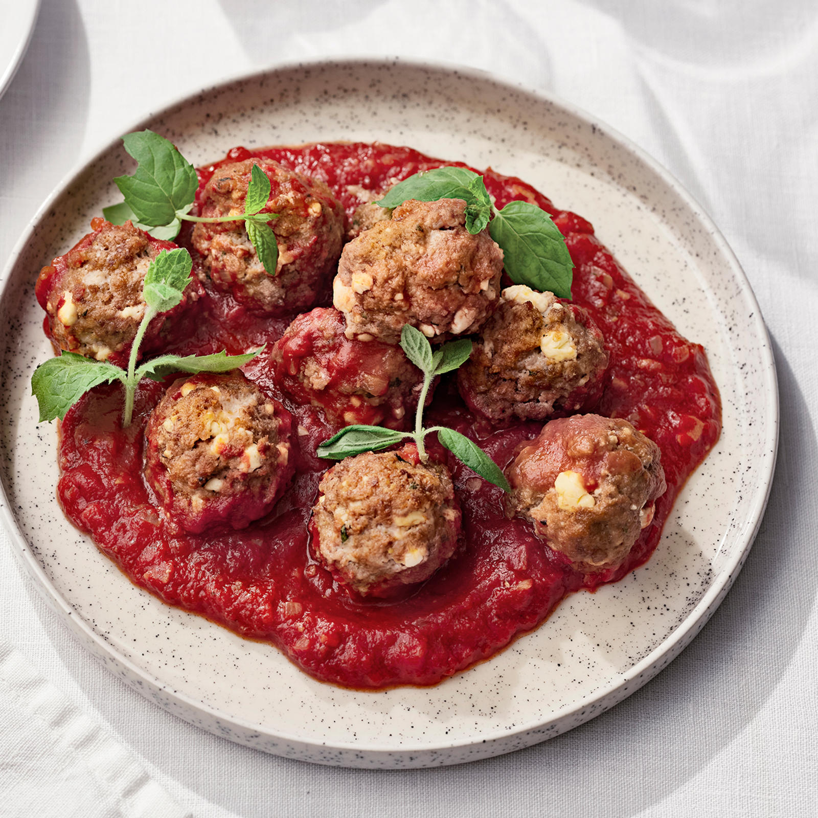 Feta-karitsapullat tomaattikastikeessa vaalealla lautasella mintunlehdillä koristeltuna.