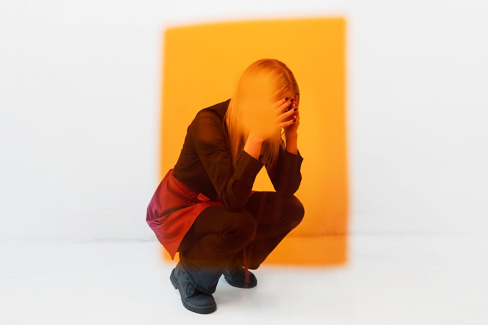 Henkilö kyykkyyn kumartuneena kädet ohimoilla.