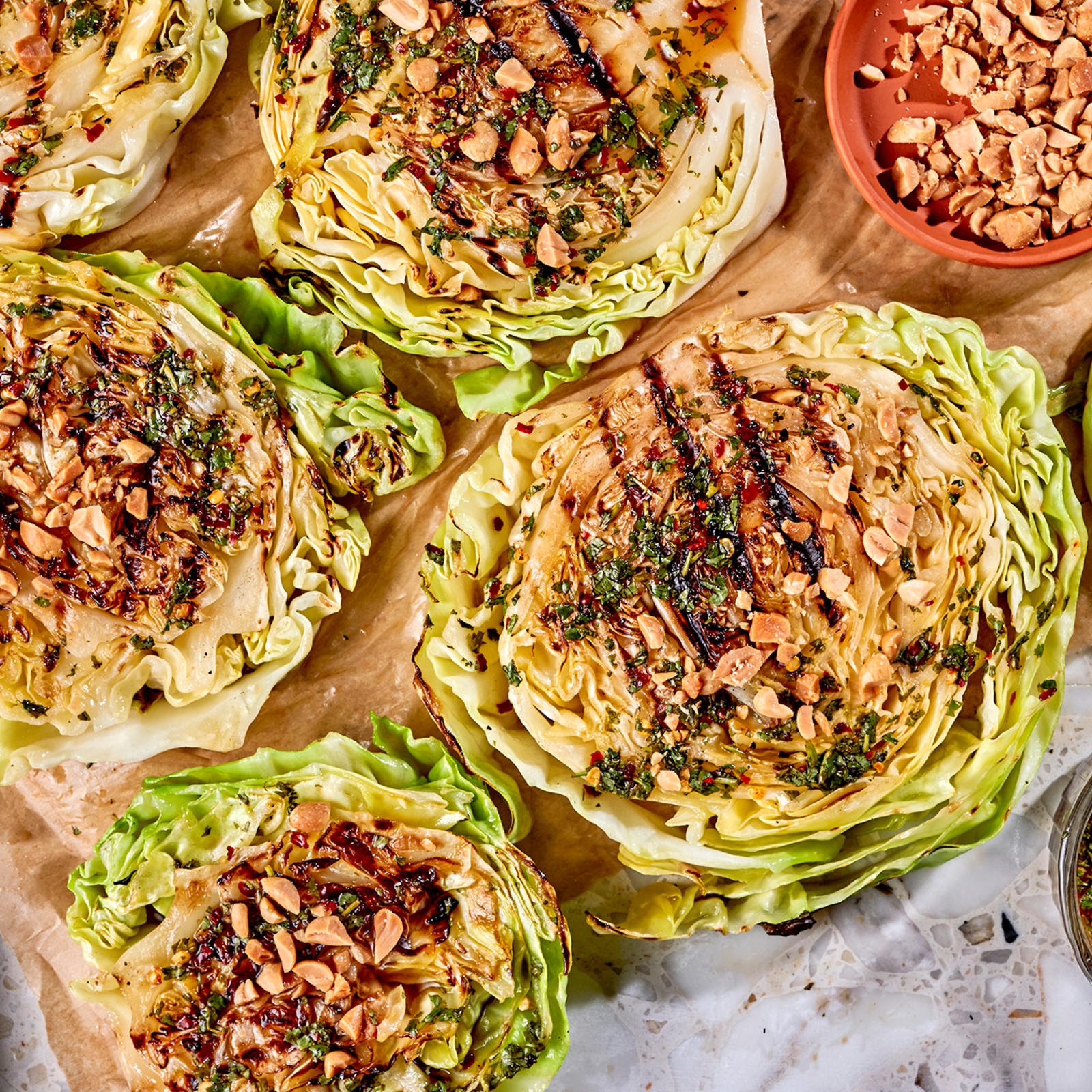 Grillattu varhaiskaali chili-sitruunakastikkeella. Vieressä paistinlasta sekä kastiketta ja suolapähkinöitä omissa kulhoissaan.