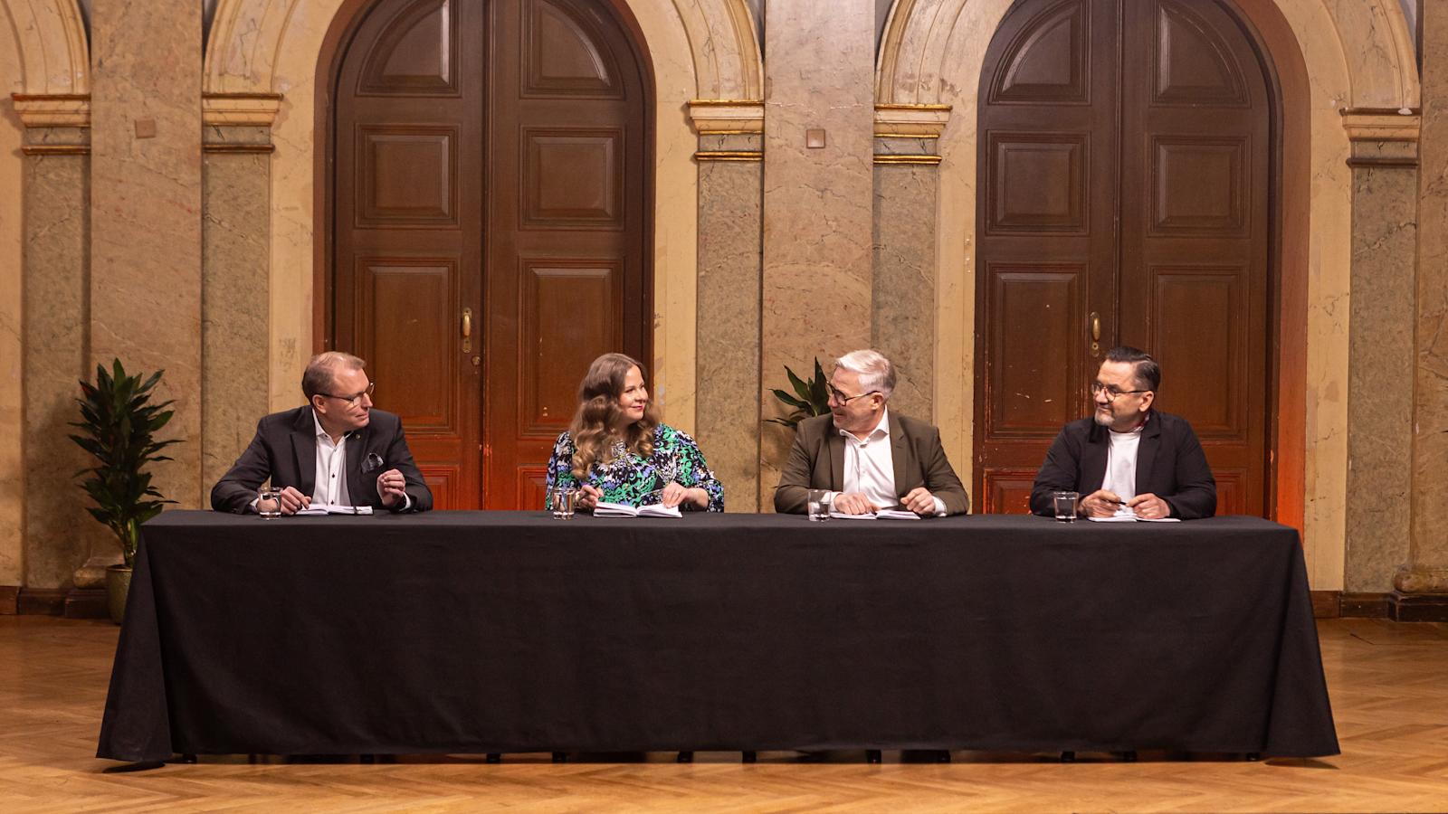 Tuomarit istuvat pöydän takana, katsovat toisiaan ja hymyilevät.