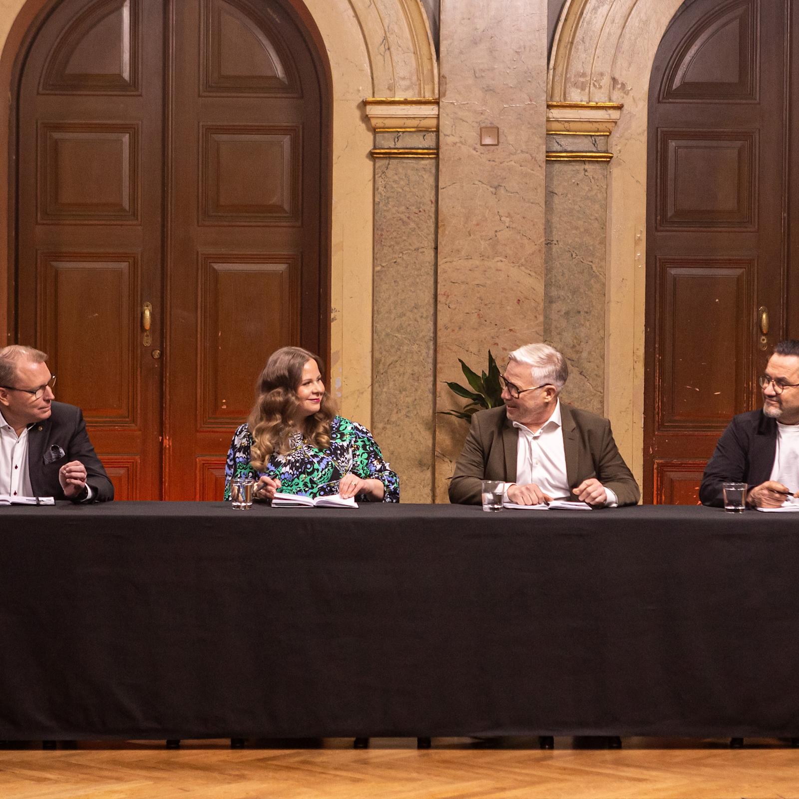 Tuomarit istuvat pöydän takana, katsovat toisiaan ja hymyilevät.