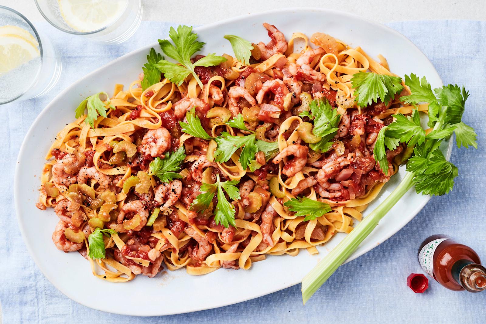 Tomaattinen katkarapupasta tarjoiluastialla varsisellerinlehdillä koristeltuna. Vieressä tabascopurkki ja kaksi vesilasia, joissa sitruunaviipaleet.