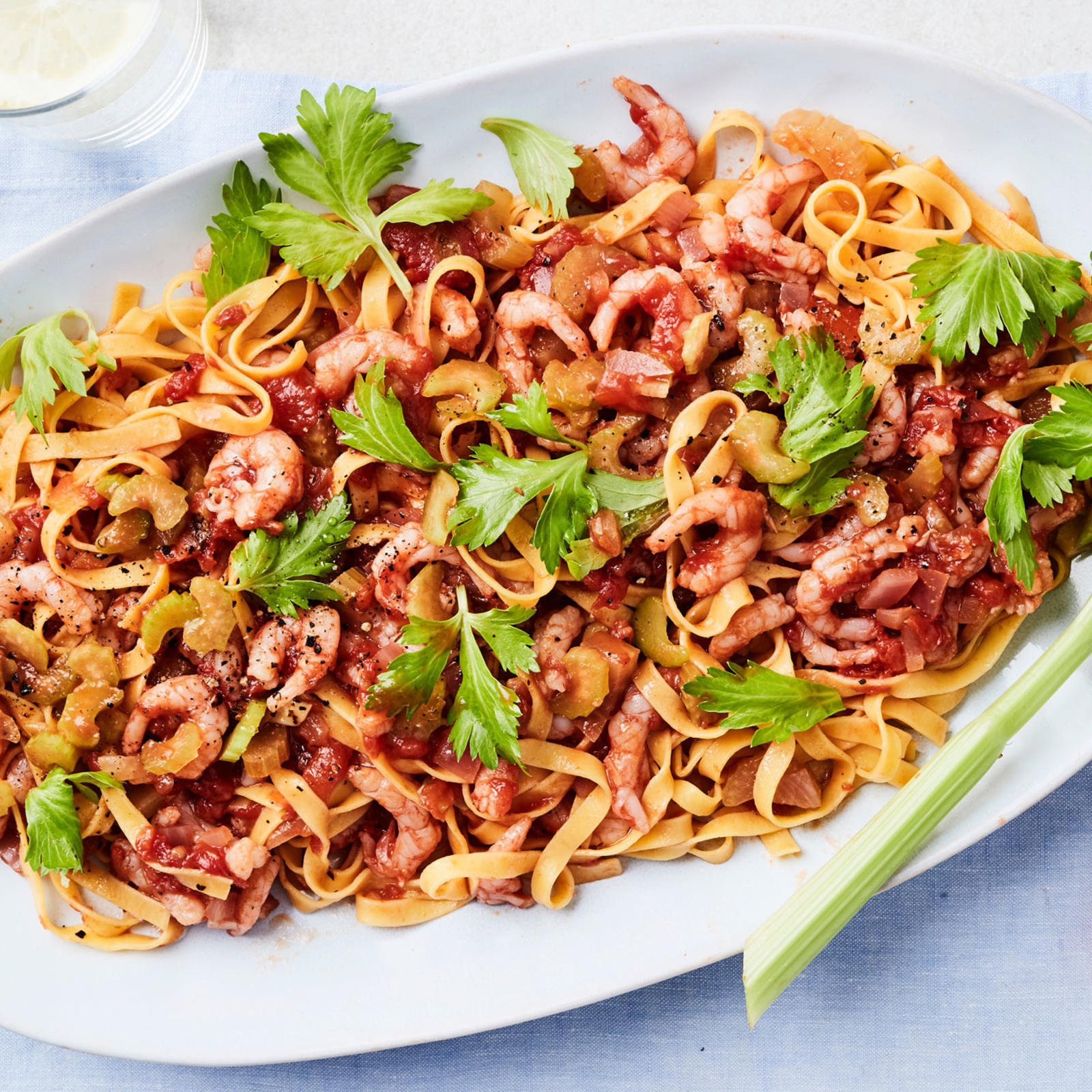 Tomaattinen katkarapupasta tarjoiluastialla varsisellerinlehdillä koristeltuna. Vieressä tabascopurkki ja kaksi vesilasia, joissa sitruunaviipaleet.