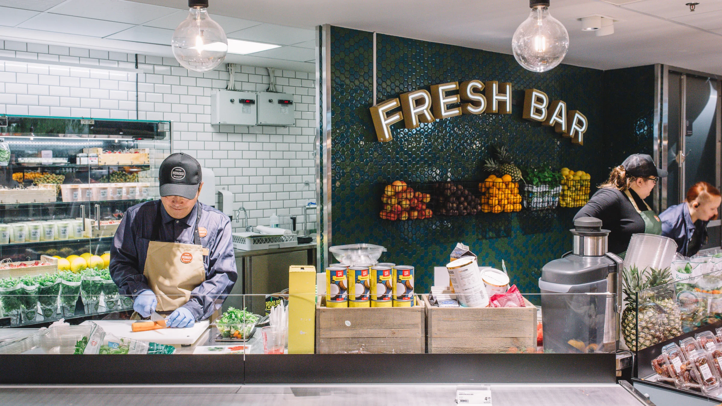 Food Market Herkun palvelutiskin takana neljä asiakaspalvelijaa touhuaa