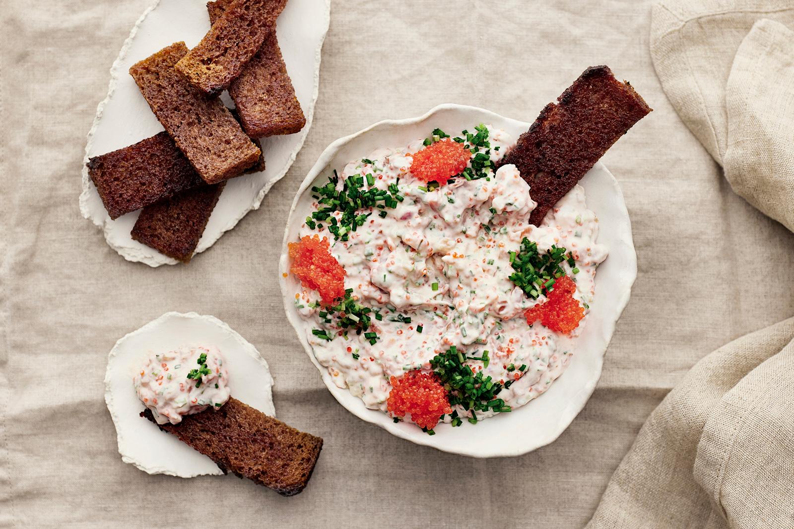 Vegaanista skagenia kulhossa merilevävalmisteella ja ruohosipulilla koristeltuna. Kulhoon dipattuna yksi leipätikku. Lisää leipätikkuja lautasilla kulhon vierellä.