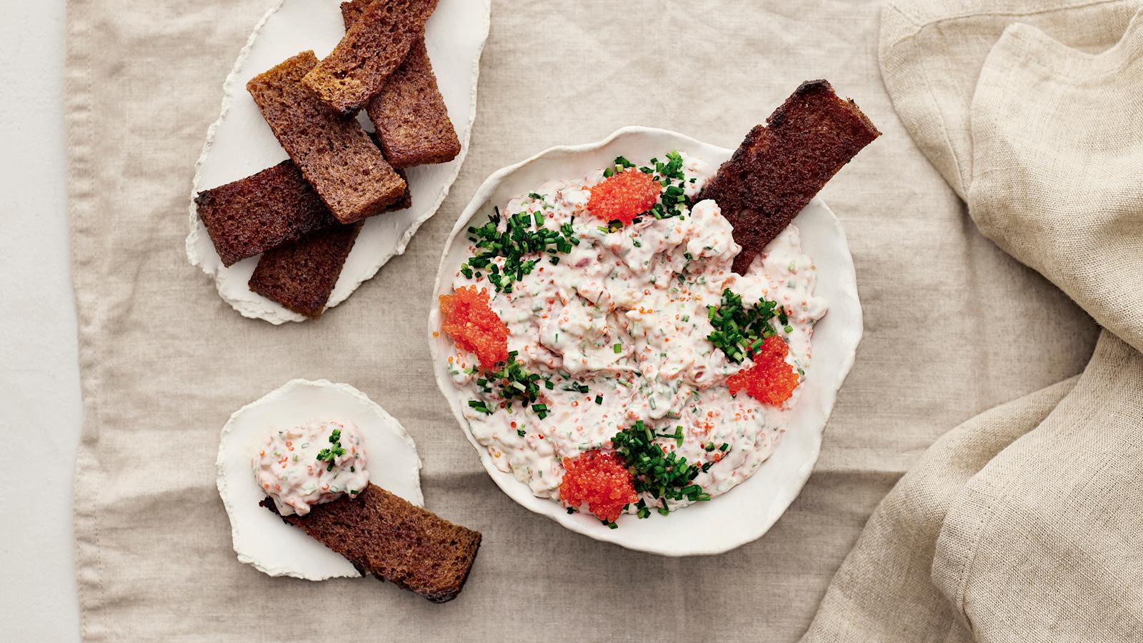 Vegaanista skagenia kulhossa merilevävalmisteella ja ruohosipulilla koristeltuna. Kulhoon dipattuna yksi leipätikku. Lisää leipätikkuja lautasilla kulhon vierellä.