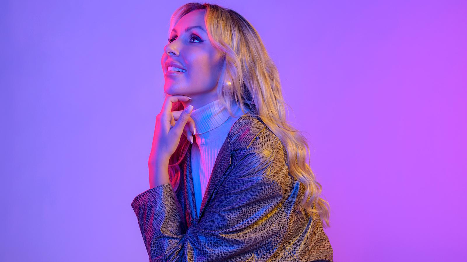 Sointu Borg katselee yläviistoon käsi leualla kirkkaan värisellä taustalla