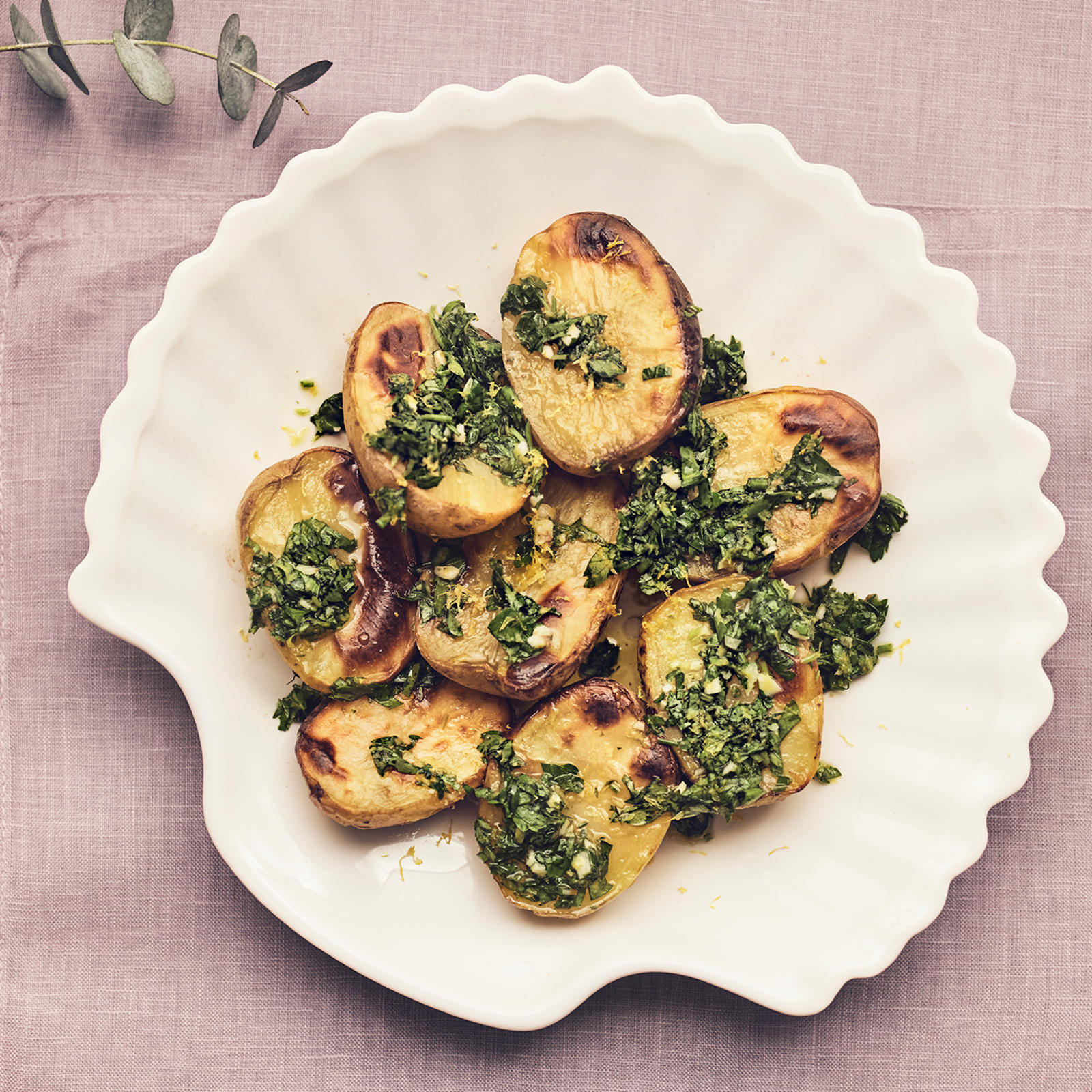 Gremolata-uuniperunat vaalealla lautasella. Lautasen alla vaaleanliila liina ja vieressä eukalyptuksen oksia.