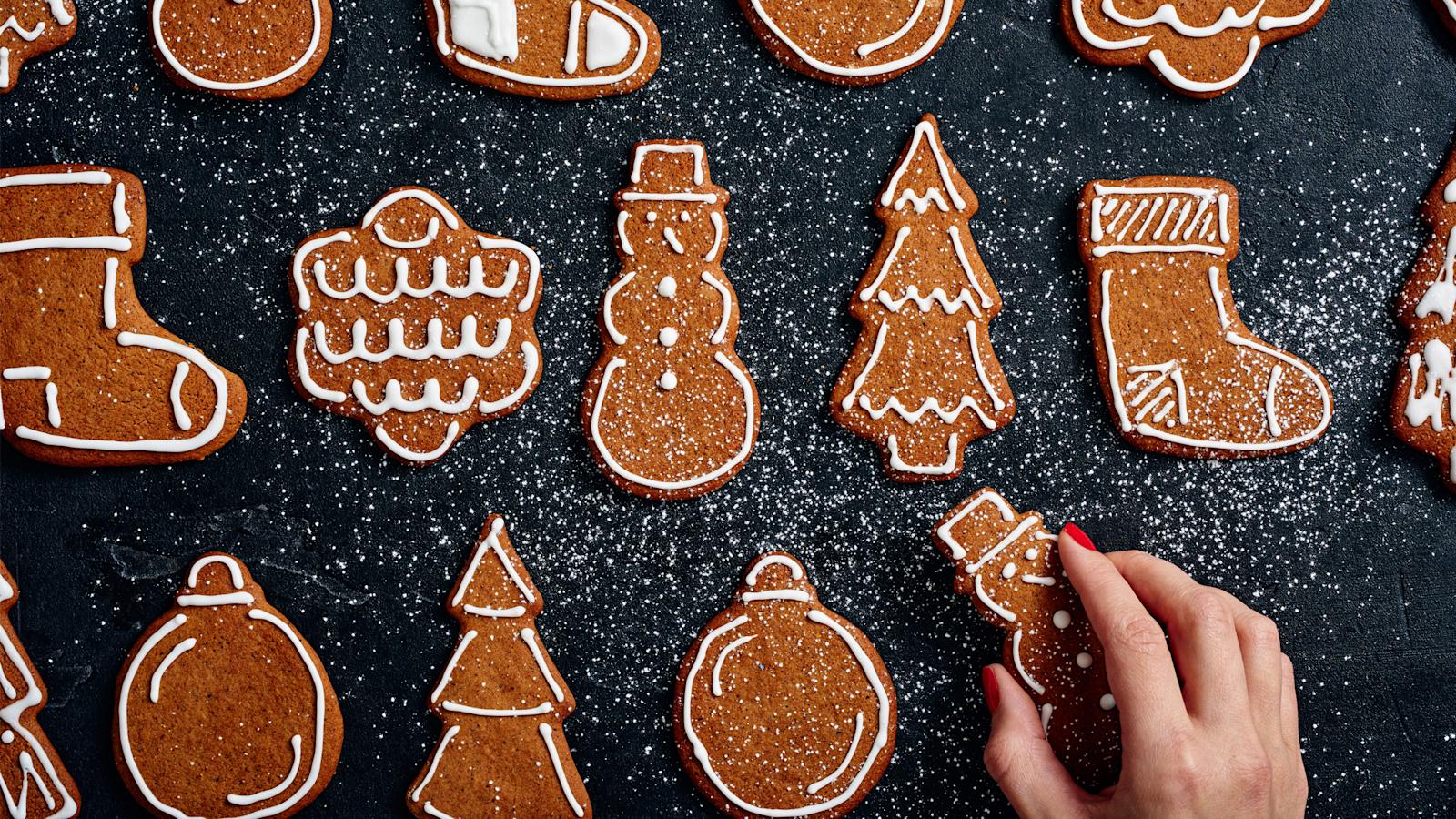 Koristeltuja pipareita mustalla alustalla. Alareunassa käsi nappaamassa piparin.