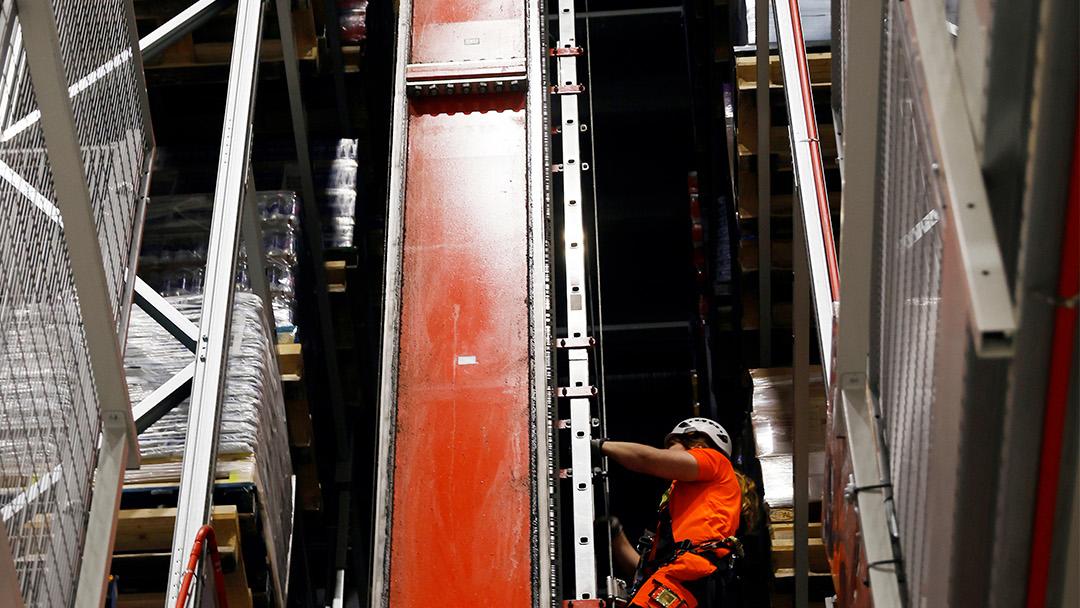 Kypäräpäinen ja turvavaljaisiin pukeutunut mies kiipeää logistiikkakekuksessa korkeaan säilytystorniin