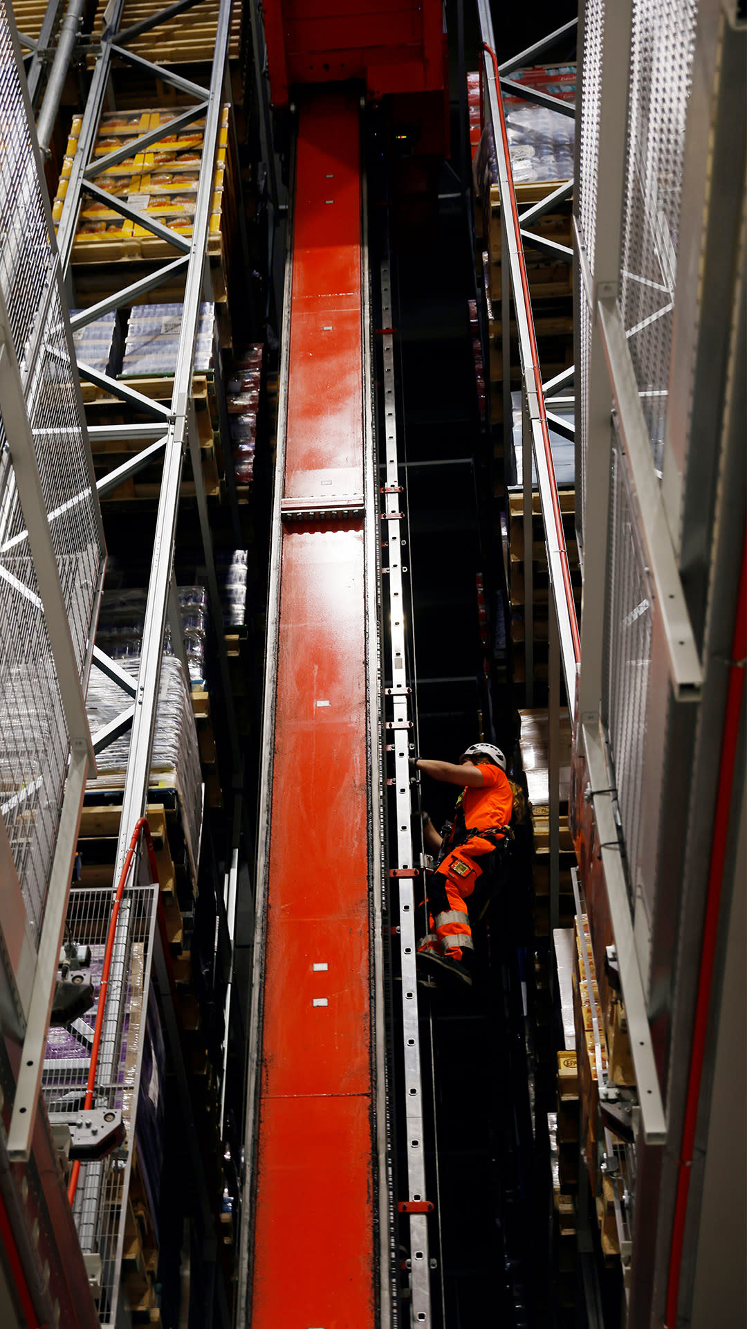 Kypäräpäinen ja turvavaljaisiin pukeutunut mies kiipeää logistiikkakekuksessa korkeaan säilytystorniin