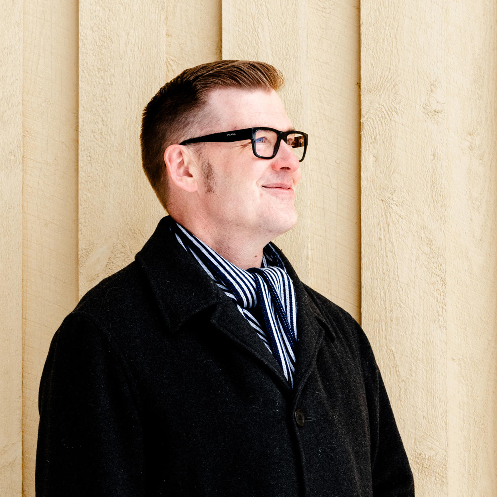 Timo Lajunen seisoo puisen seinän edustalla hymyillen.