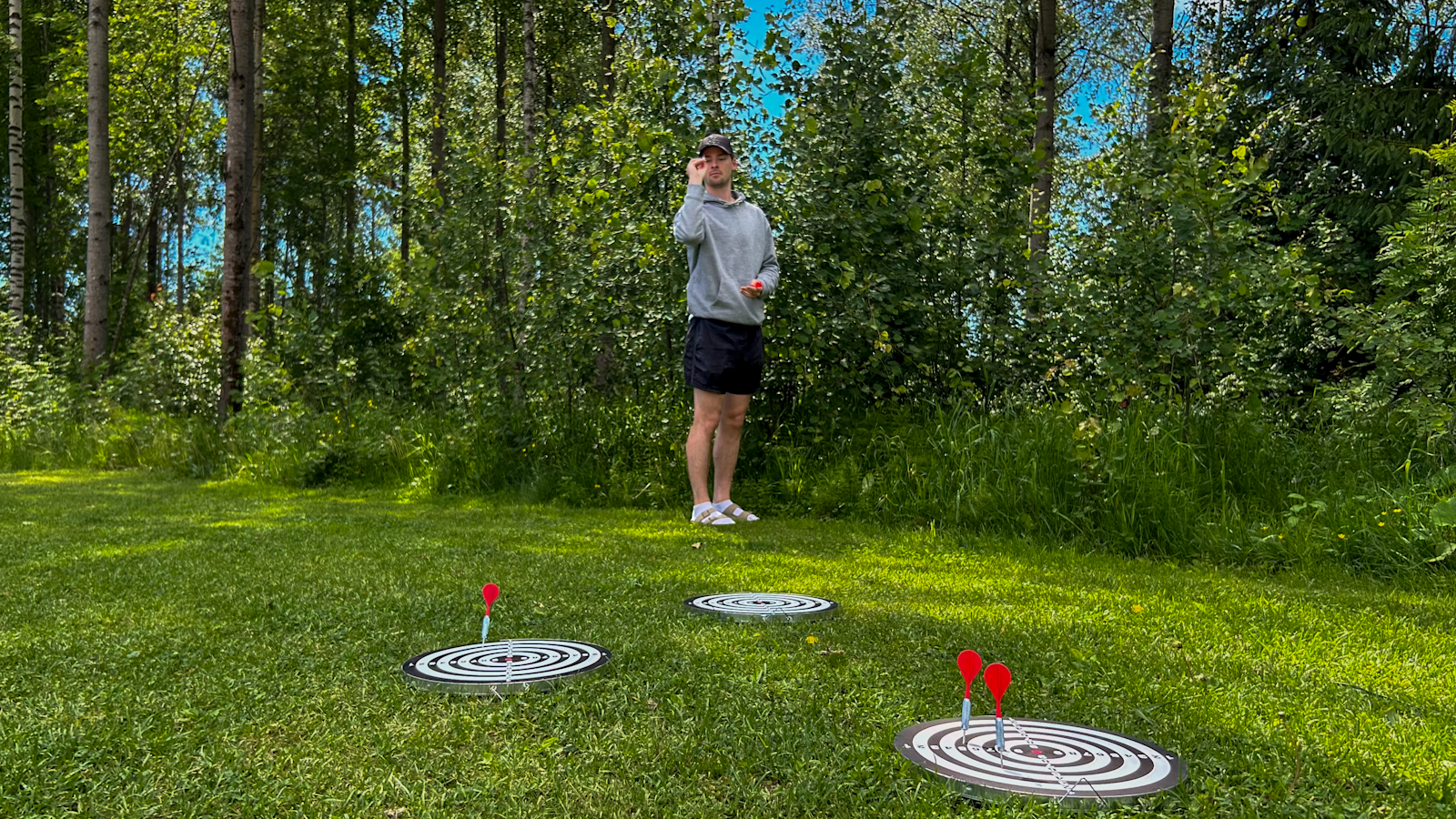 Nurmikolla on kolme tikkataulua, joihin heittäjä yrittää osua. Yhdessä taulussa on kiinni kaksi tikkaa.