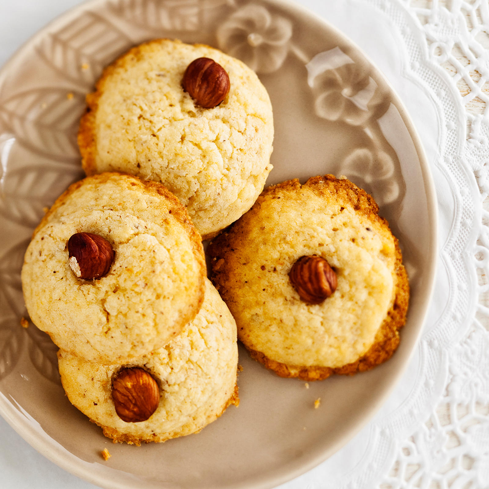 Vaaleita hasselpähkinäpipareita lautasella. Alla valkoinen pitsiliina.