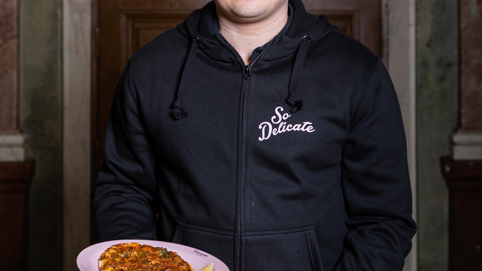 Spiros Halaris pitelee käsissään kahta lautasta, joilla on hiivatonta ohutleipää. Päällä musta paita ja jalassa siniset farkut.