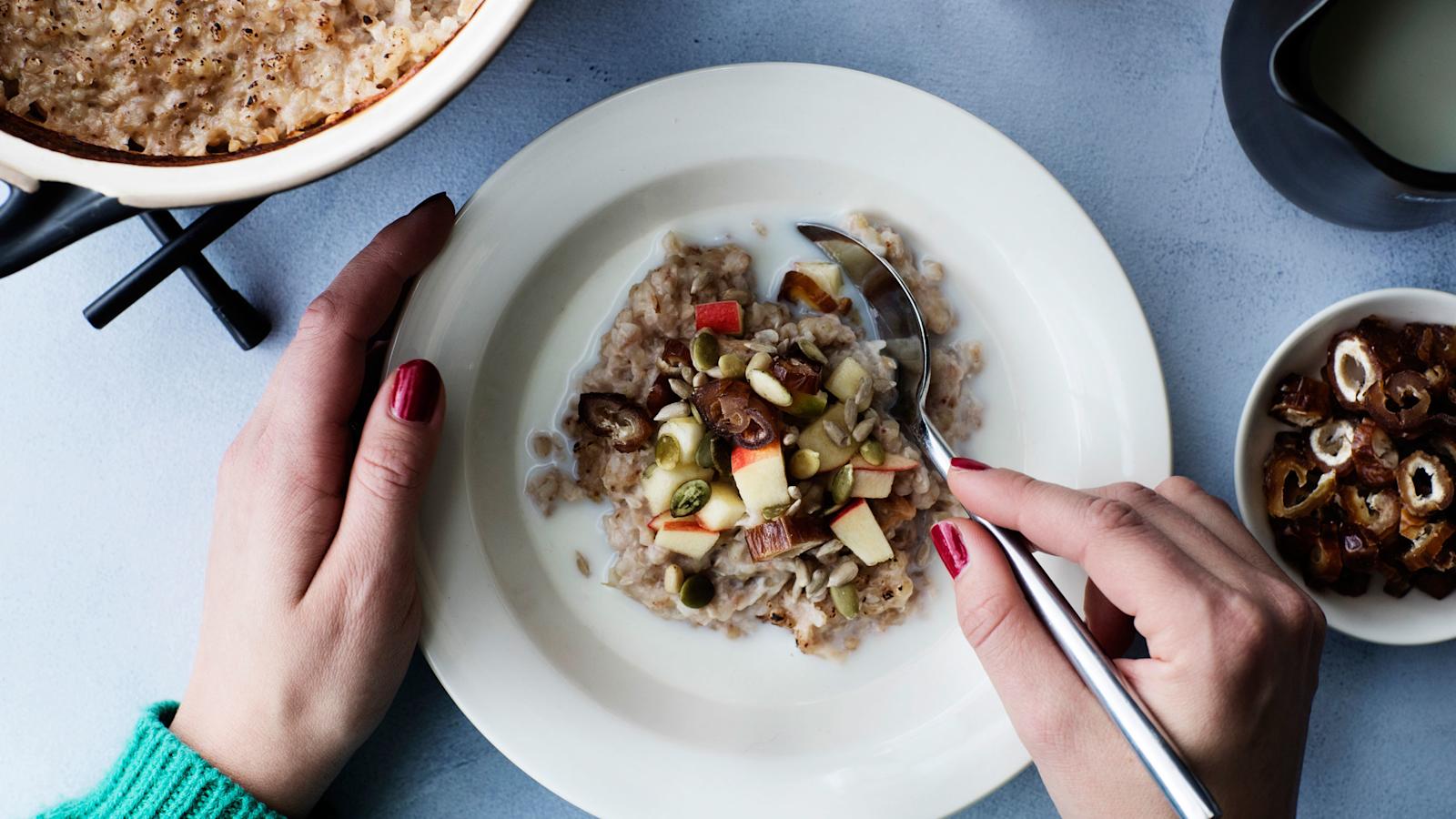 Tattaripuuroa valkoisella lautasella., puuron päällä lisukkeita. Käsiä pitää lusikkaa, joka upotettu puuroon.