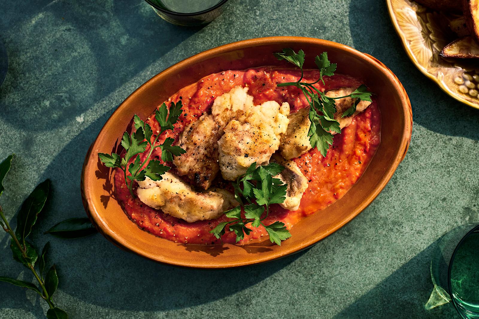 Paistettua seitiä ja paprikakastiketta oranssissa tarjoiluastiassa. Päällä lehtipersiljan oksia.