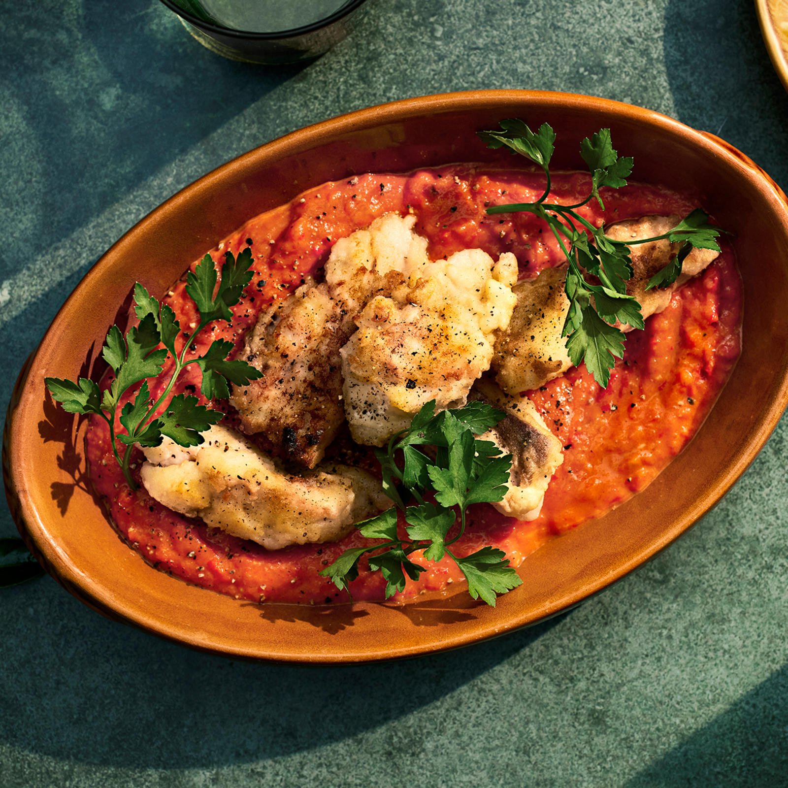 Paistettua seitiä ja paprikakastiketta oranssissa tarjoiluastiassa. Päällä lehtipersiljan oksia.