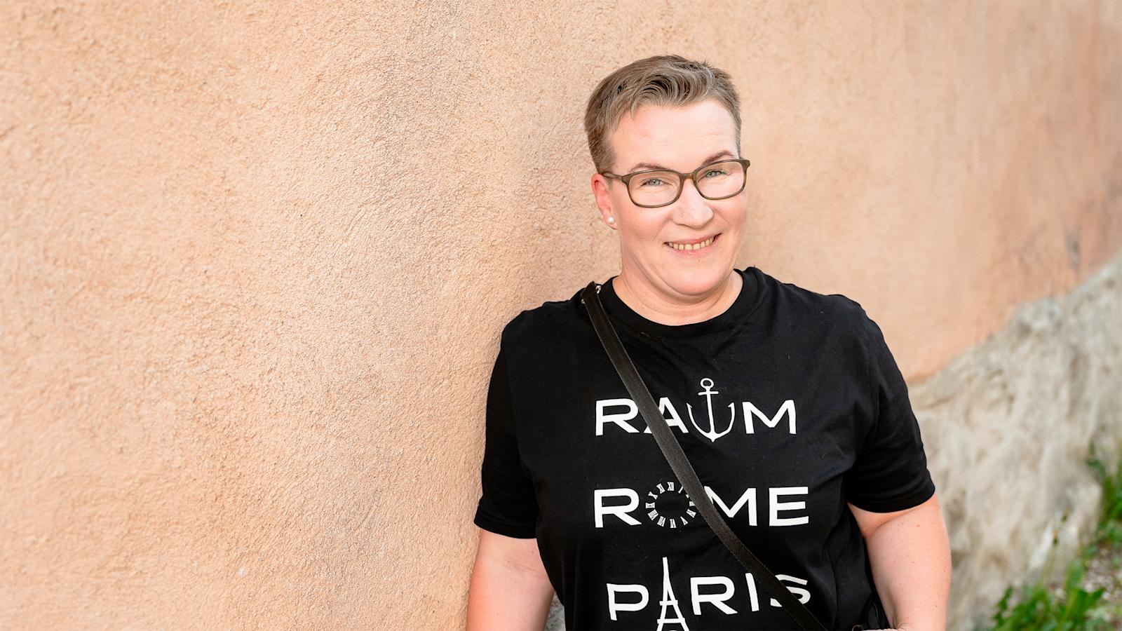 Tiiliseinään nojaava nainen hymyilee