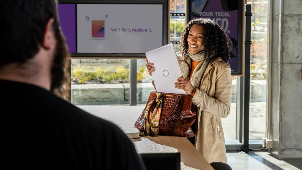 Woman walking into Asurion Tech Repair & Solutions store holding laptop computer