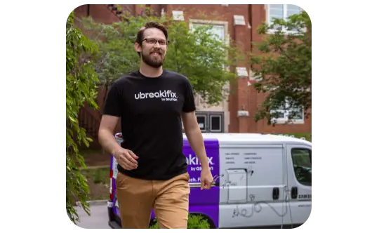 A smiling uBreakiFix by Asurion technician walking toward a home with a branded van parked behind him