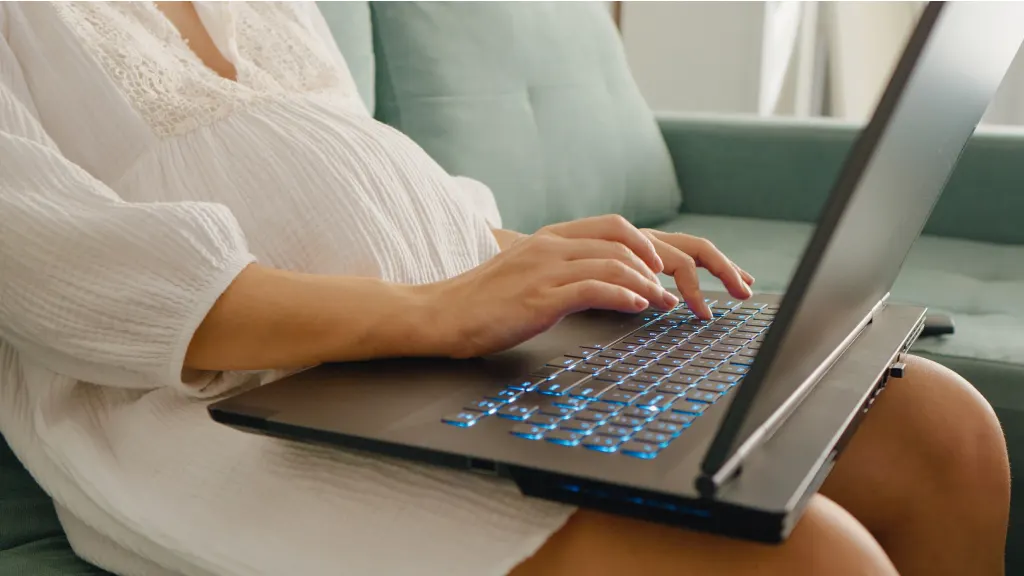 Pregnant woman in a white dress typing on a laptop in her lap