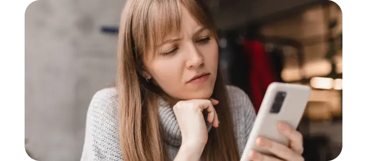 Woman looking thoughtfully at her smartphone, representing app management, troubleshooting, and deciding which apps to keep or delete.