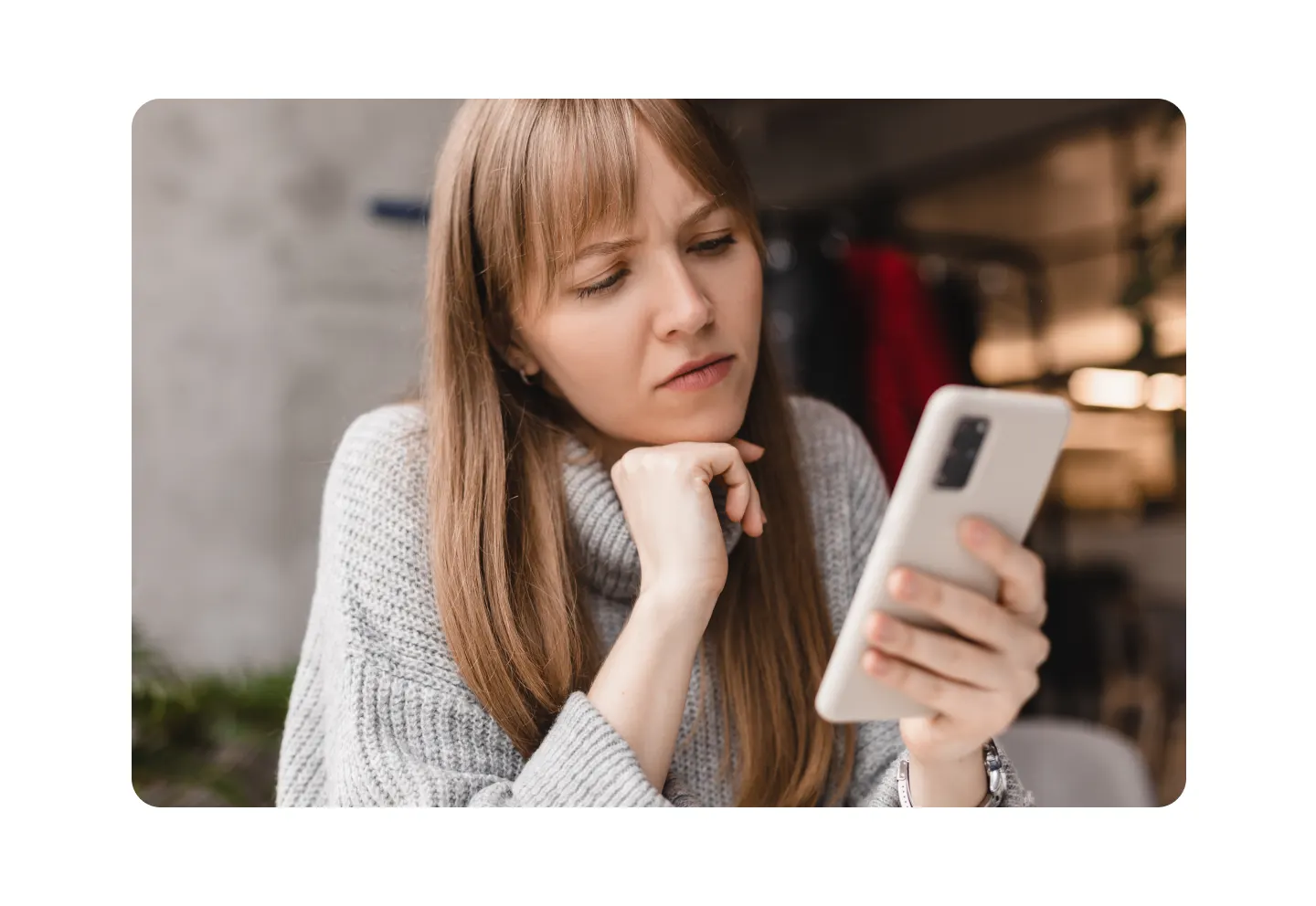 Woman looking thoughtfully at her smartphone, representing app management, troubleshooting, and deciding which apps to keep or delete.