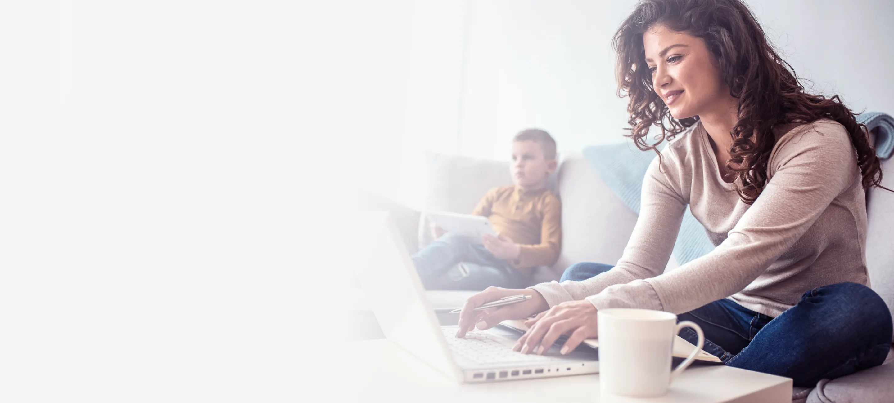 Woman sitting on a couch with a child, working on her laptop