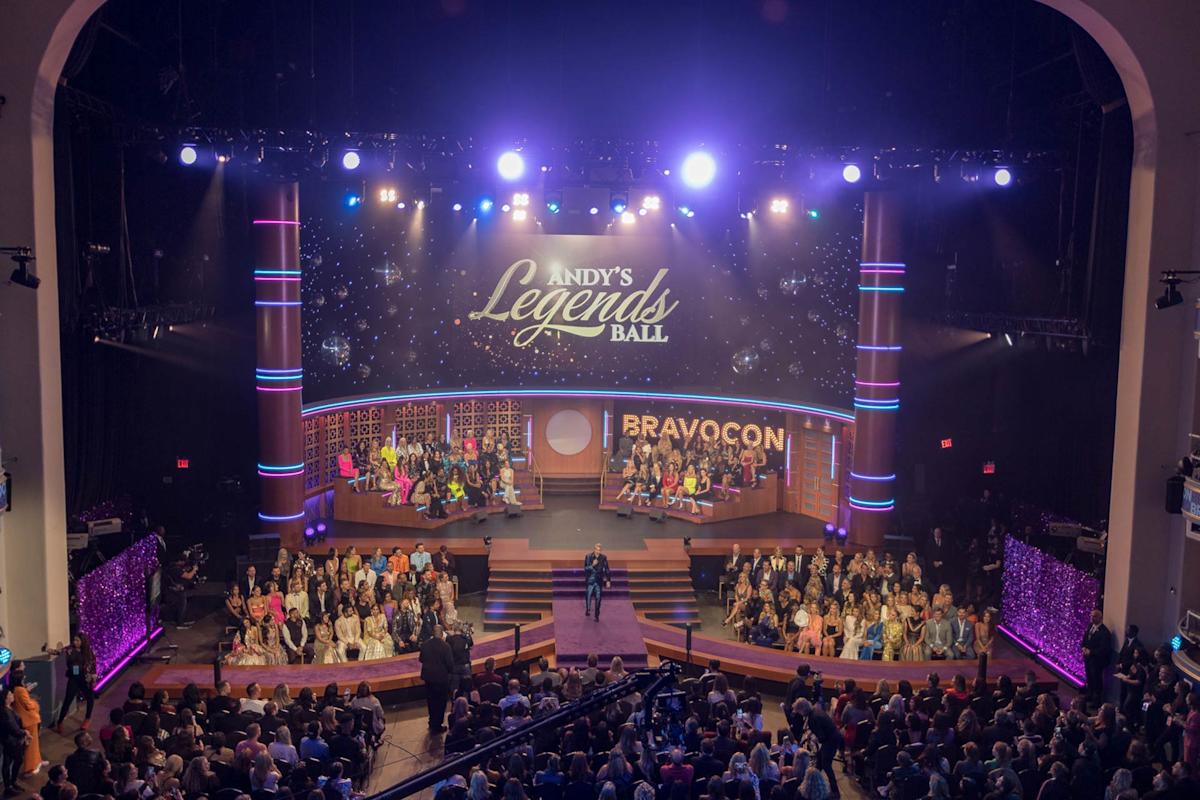 A large, brightly lit stage at BravoCon features a backdrop reading "Andy's Legends Ball." The audience fills the theater while people are seated and standing on stage, surrounded by colorful lights and decor.