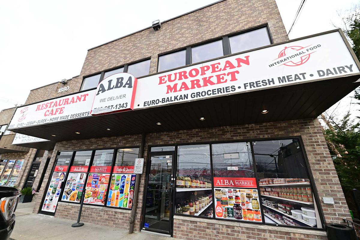 A two-story brick building with signs reading "ALBA European Market," "Restaurant Cafe," and "Euro-Balkan Groceries, Fresh Meat, Dairy." The storefront displays food posters and shelves with various products inside.