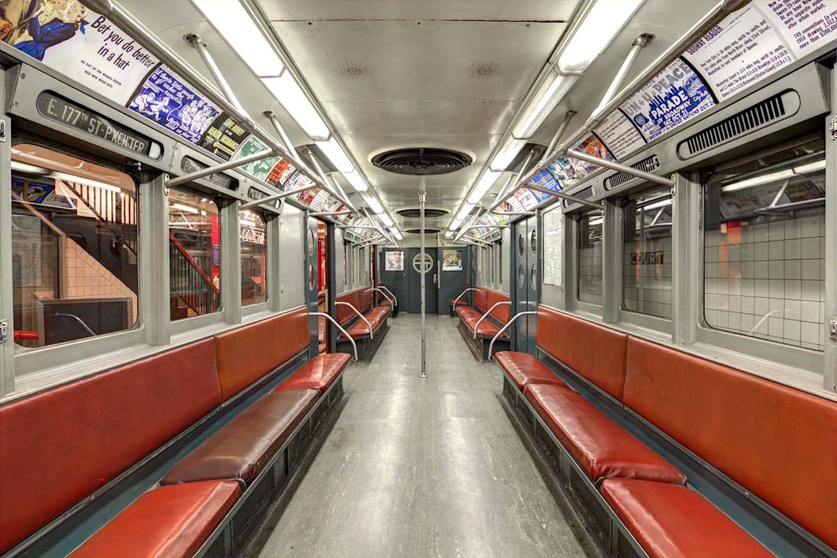 Interior of a vintage subway car with brown leather seats lining both sides. The car is empty, with advertisement panels above the windows. The lighting is bright, and there's a silver ventilation fan on the ceiling.