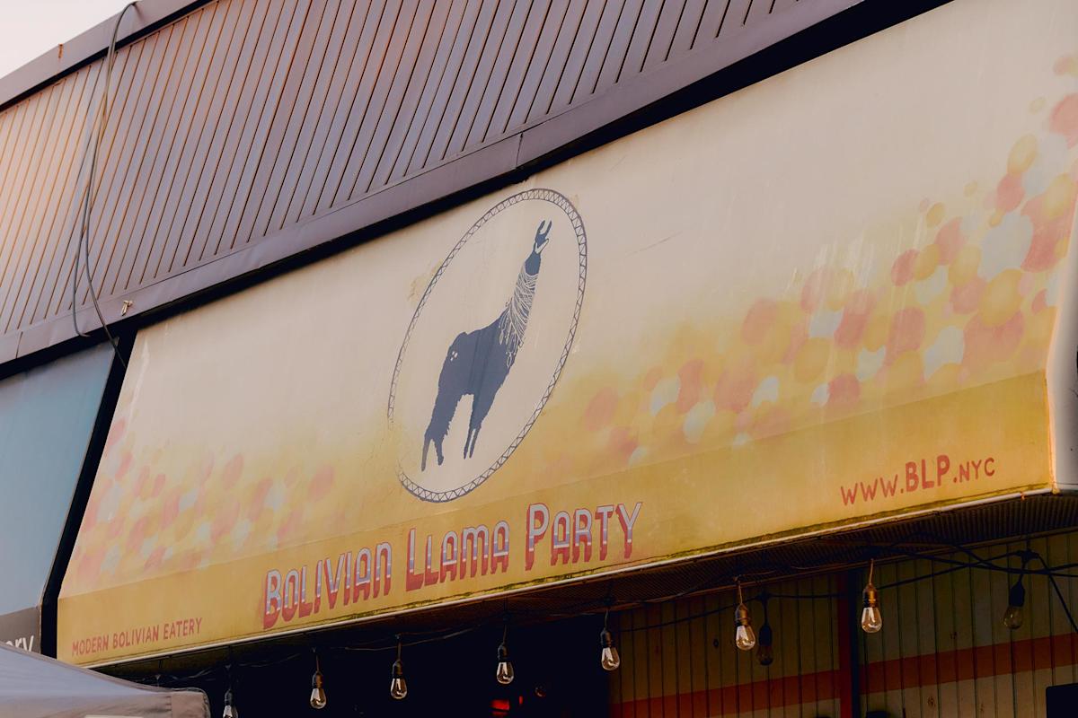 A restaurant sign features a llama illustration with the text “Bolivian Llama Party” in bold letters. The background is yellow with colorful dots, and the website “www.BLP.nyc” is displayed on the right.