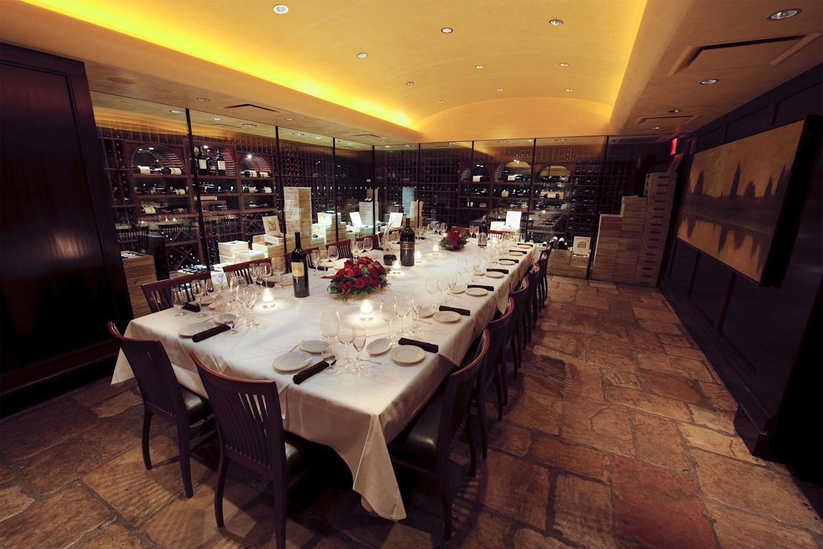 A long dining table with a white tablecloth is elegantly set for a meal in a dimly lit, upscale restaurant, surrounded by wine racks and decorative elements.