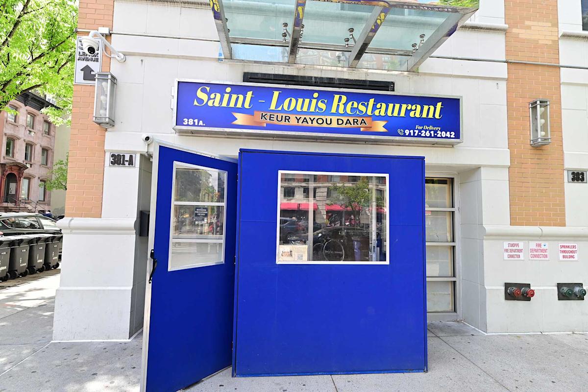 The exterior of Saint-Louis Restaurant, a Senegalese eatery, with a blue entry structure and a sign above the door. The address number 391A is visible on the white and brick building.