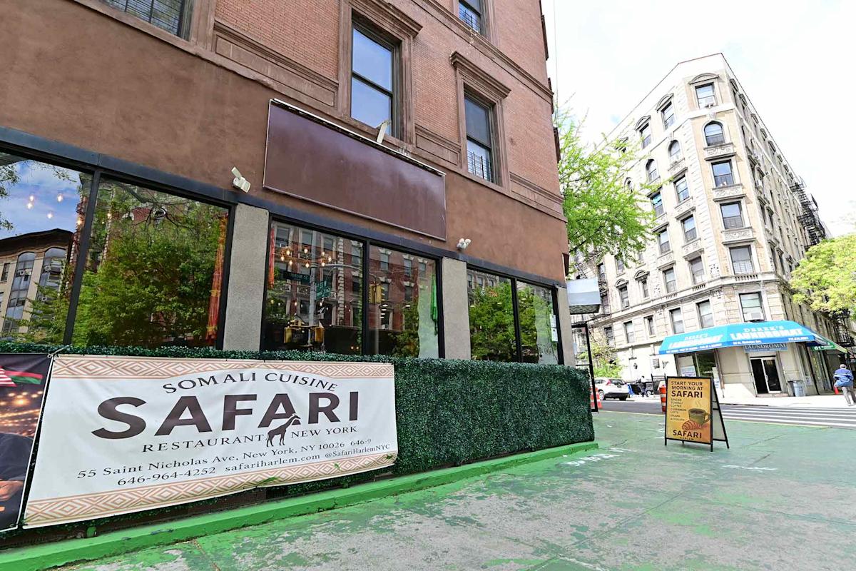 A Somali restaurant called Safari, with a large banner displaying its name and address, is on a city street corner. The building is brown with large windows, and a blue awning is visible across the intersection.