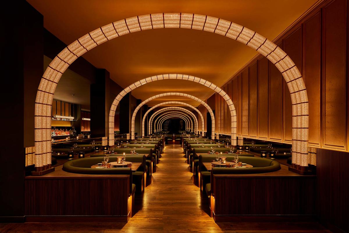 Elegant restaurant interior with warm lighting, featuring multiple illuminated arches over rows of green booth seating and neatly set tables, creating a cozy and inviting dining atmosphere.