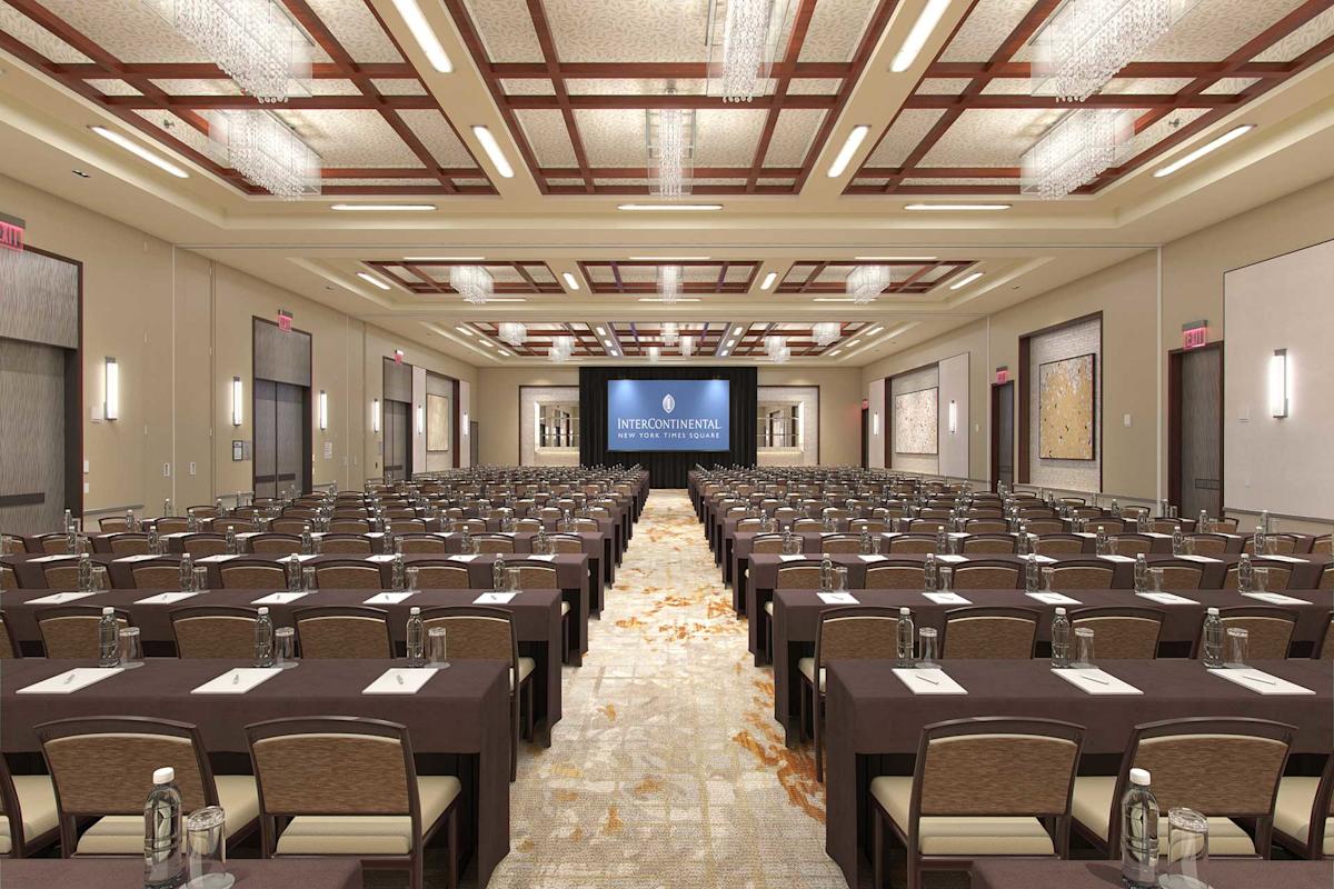 A large, elegant conference room set up classroom-style with rows of tables and chairs facing a stage and large screen displaying “InterContinental.” Notepads and water bottles are placed on each table.