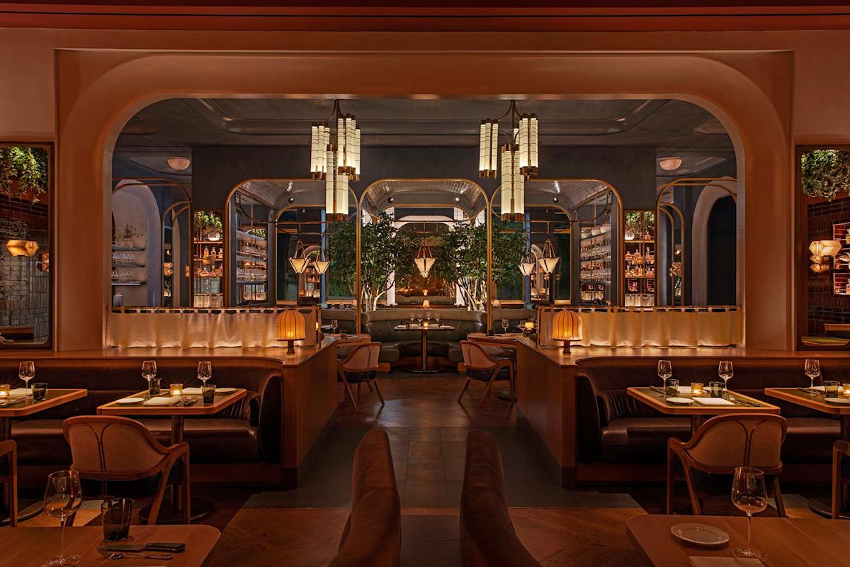 A stylish, modern restaurant interior with warm lighting, cozy booths, elegant tables set with glassware, greenery, and art deco-inspired decor, creating an inviting and sophisticated dining atmosphere.