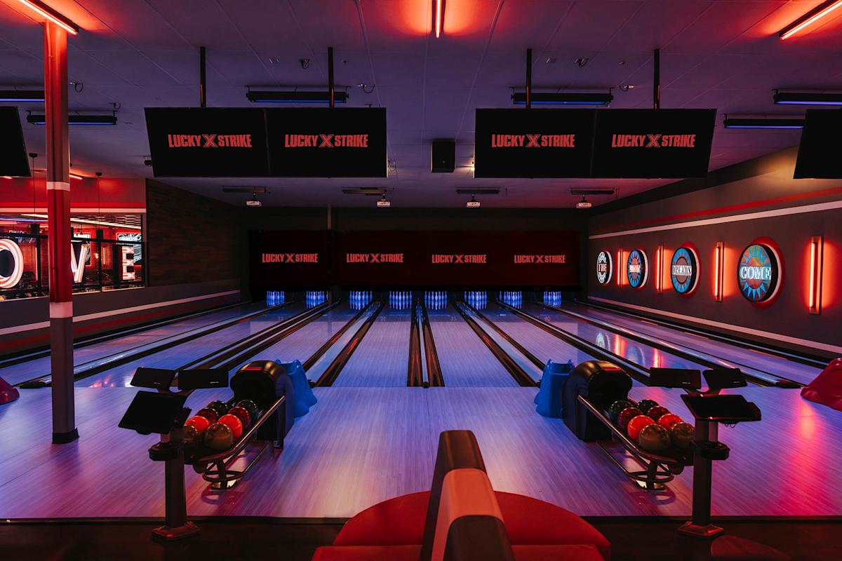 A modern bowling alley with multiple lanes, colorful bowling balls, digital screens displaying “Lucky Strike,” and vibrant lighting creating a lively atmosphere.